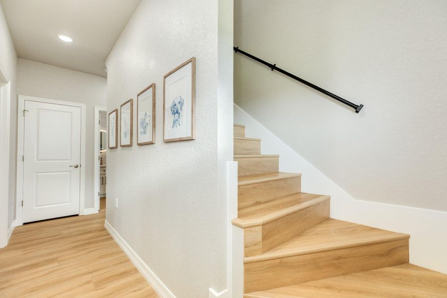 Bright hallway features durable wood-look flooring and a staircase providing easy access between levels.