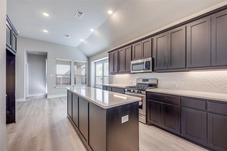 Kitchen featuring appliances with stainless steel finishes, a kitchen island, tasteful backsplash, recessed lighting, and light wood-style flooring