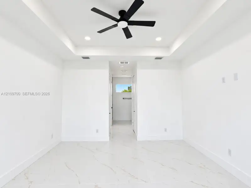 Tray ceiling featuring a matte black multi-blade ceiling fan, recessed lighting, and large-format tile flooring with veining