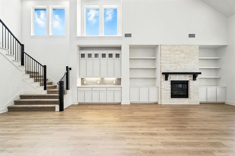 Unfurnished living room with high vaulted ceiling, a fireplace, light wood-type flooring, stairway, and built in features Unfurnished living room with high vaulted ceiling, a fireplace, light wood-type flooring, stairway, and built in features