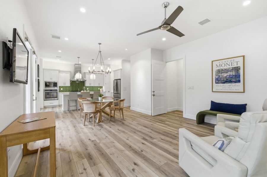 Living room with light wood-type flooring, a ceiling fan, and suspended lighting