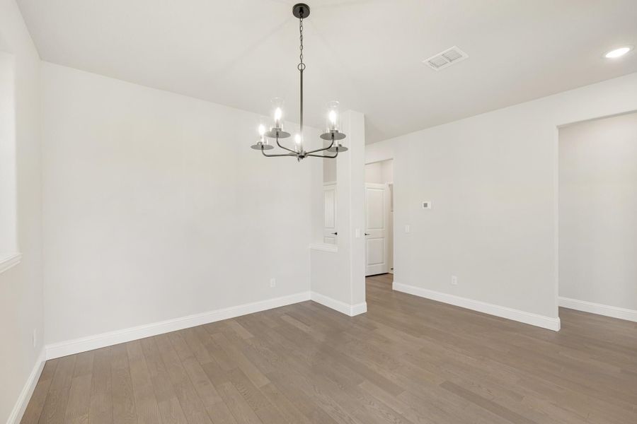 Empty dining room with dark wood floors, white walls, and a modern chandelier overhead