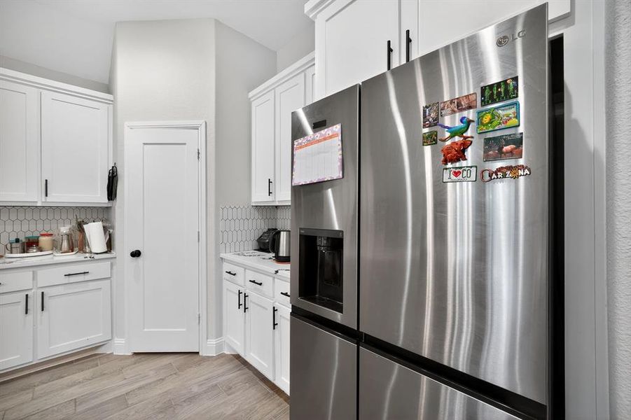 Kitchen featuring stainless steel fridge, white cabinetry, light countertops, and light wood-style floors