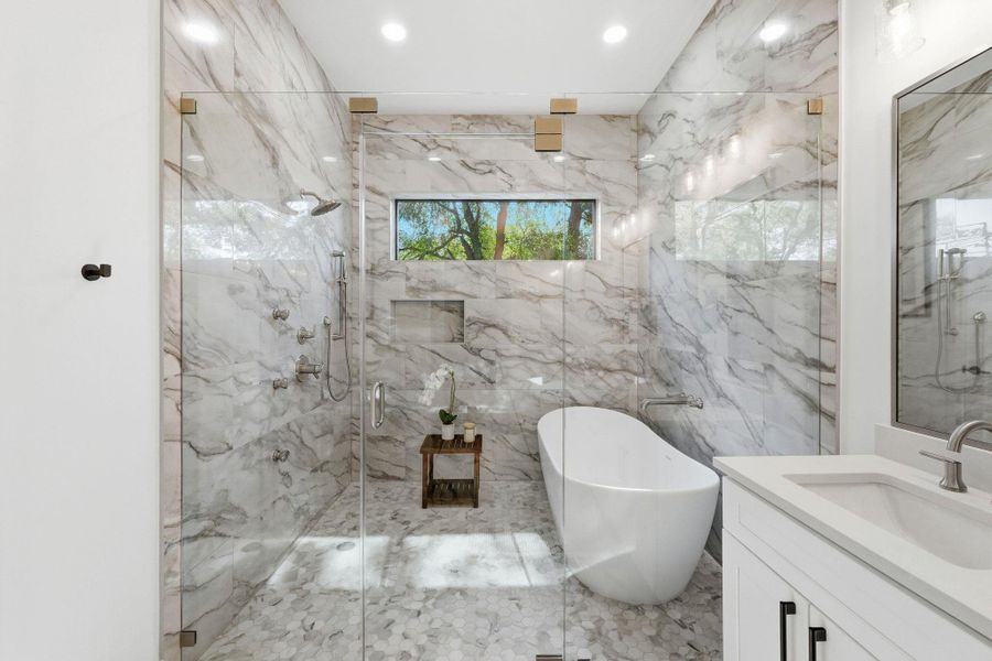 Primary bathroom with a freestanding tub, vanity, a marble finish shower, tile walls, and recessed lighting Primary bathroom with a freestanding tub, vanity, a marble finish shower, tile walls, and recessed lighting