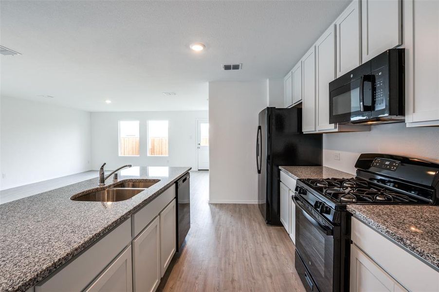 Kitchen with black appliances, white cabinetry, stone countertops, sink, and light hardwood / wood-style flooring