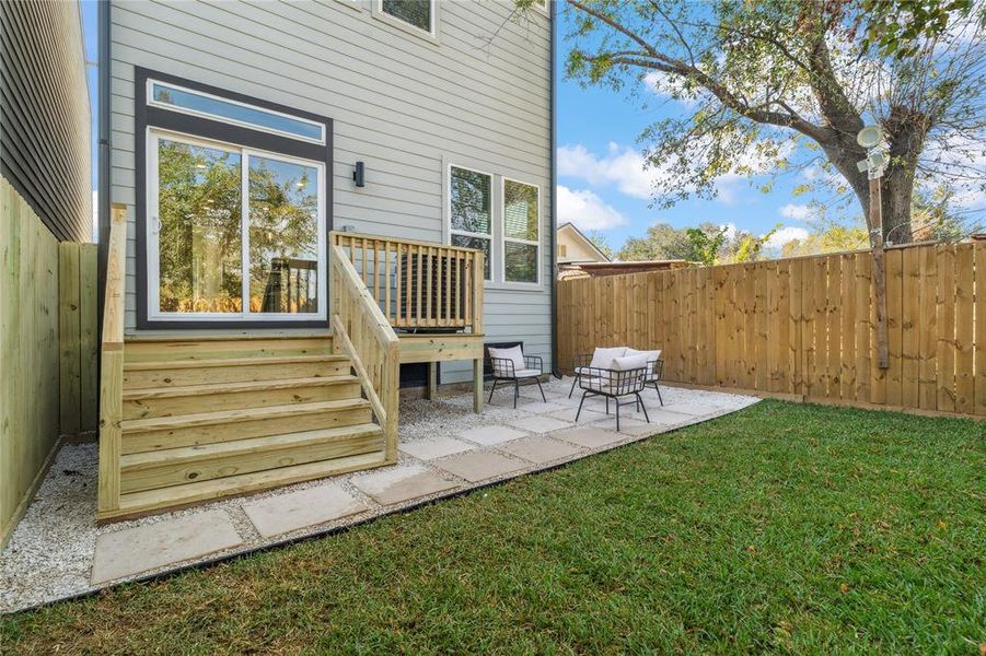 Inviting backyard featuring a freshly built deck, a charming seating area on a paved patio, and a lush green lawn enclosed by a privacy fence, ideal for outdoor enjoyment