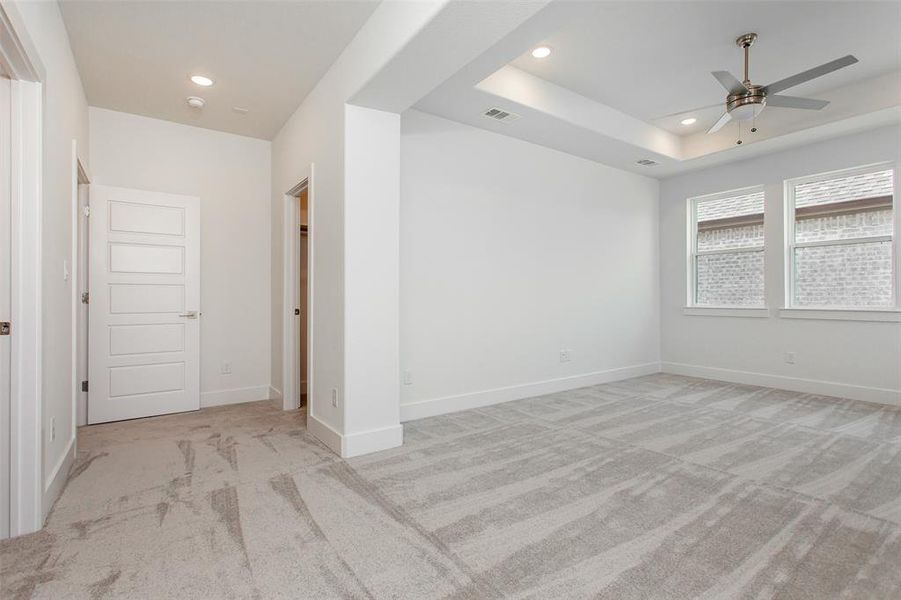 Unfurnished room featuring ceiling fan, light carpet, and a tray ceiling