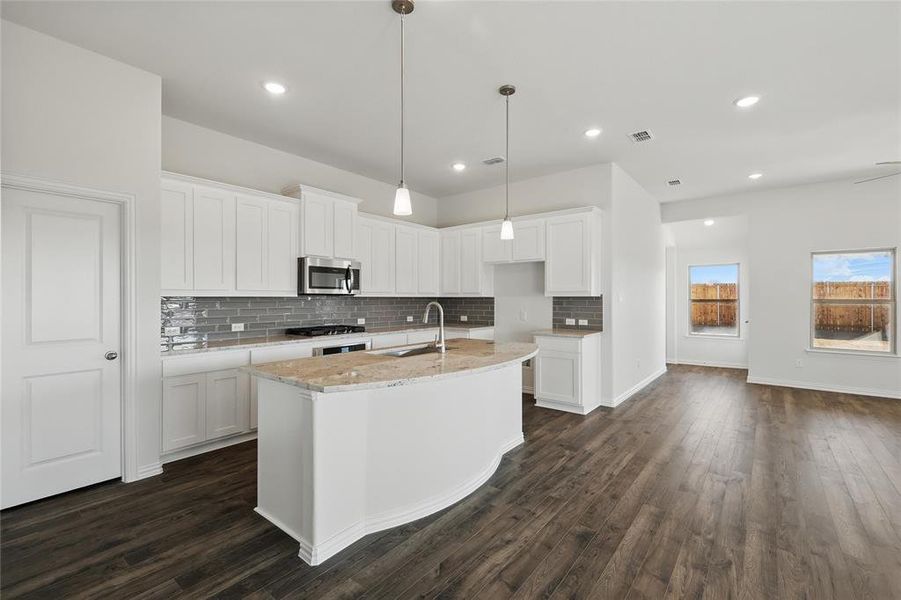 Kitchen featuring a center island with sink, white cabinetry, light stone counters, stainless steel microwave, and dark wood-type flooring