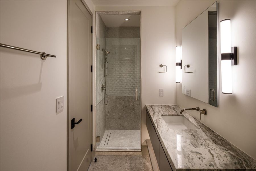 Another beautifully finished private ensuite with a stone-topped floating vanity, wall-mounted fixtures, oversized mirror, and glass-enclosed shower. Even the secondary baths make a statement.
