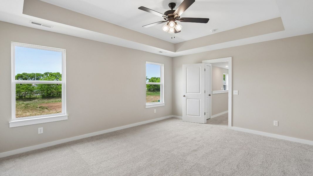 Bedroom with tray ceiling, windows, and en-suite primary bathroom