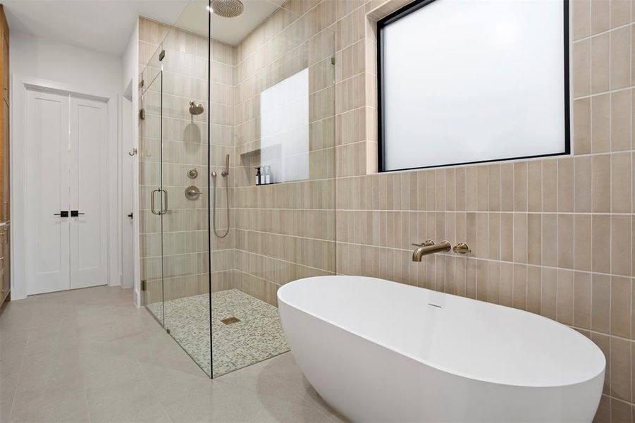 Modern bathroom featuring a freestanding soaking tub, a frameless glass shower enclosure with pebble flooring, and vertical tile accents