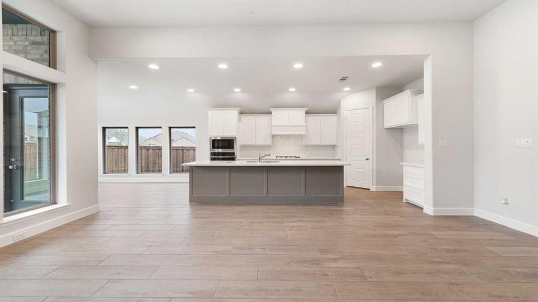 Kitchen with white cabinetry, stainless steel microwave, tasteful backsplash, an island with sink, and sink