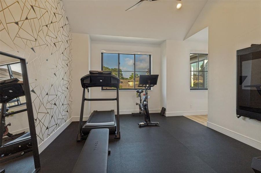 Dedicated fitness space with dark rubber flooring and an accent wall featuring a geometric pattern Dedicated fitness space with dark rubber flooring and an accent wall featuring a geometric pattern
