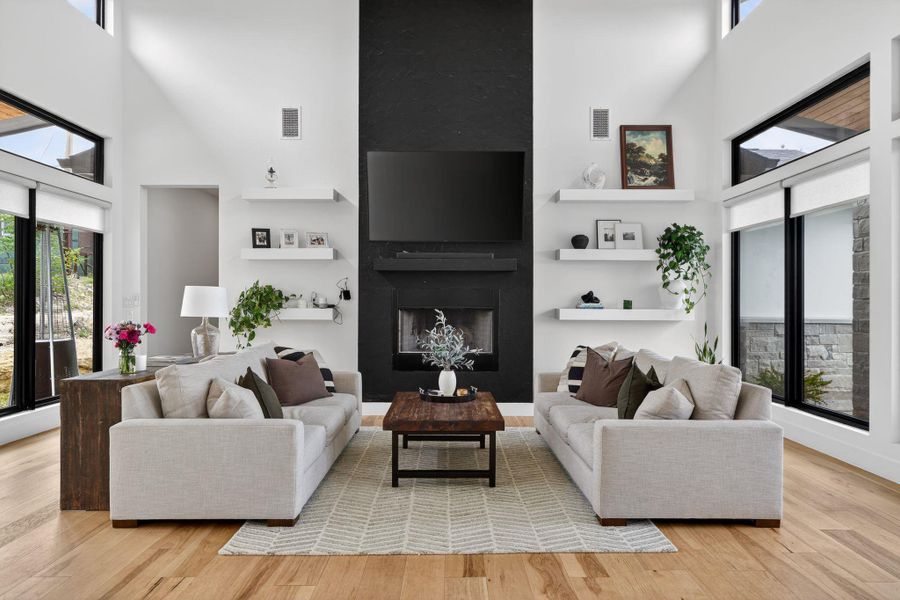 Living area with healthy amount of natural light, a high ceiling, a large wood-burning fireplace, and light wood-style floors