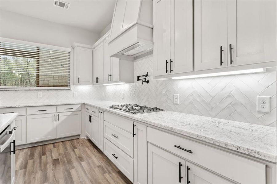 Kitchen with light hardwood / wood-style floors, tasteful backsplash, white cabinetry, appliances with stainless steel finishes, and premium range hood