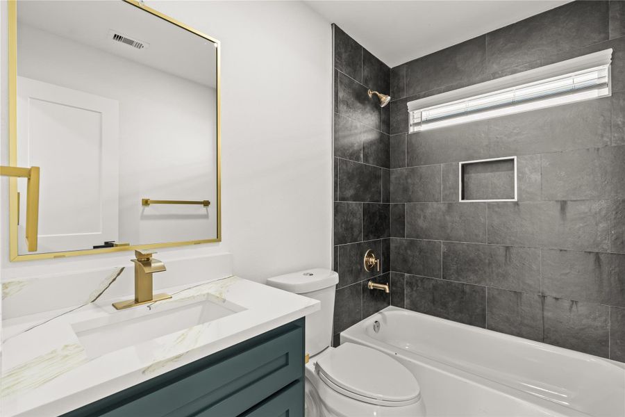 Bold, dramatic style. The full upstairs guest bathroom showcases a striking floor-to-ceiling charcoal tile accent wall paired with an elegant emerald vanity and gold hardware.