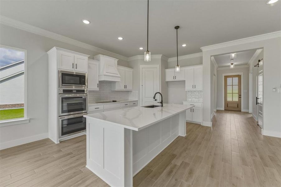 Modern kitchen featuring white cabinetry, a large center island with a sink, double wall ovens, and wood-finish flooring Modern kitchen featuring white cabinetry, a large center island with a sink, double wall ovens, and wood-finish flooring