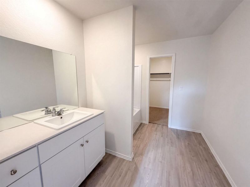 Smooth wood-look flooring leads past a white vanity to an adjoining walk-in closet.