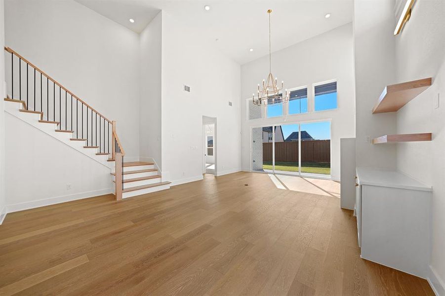 Unfurnished living room with stairway, light wood finished floors, a towering ceiling, recessed lighting, and a chandelier Unfurnished living room with stairway, light wood finished floors, a towering ceiling, recessed lighting, and a chandelier
