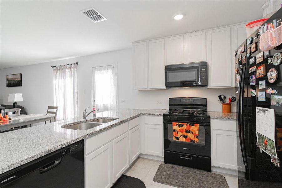 Kitchen featuring black appliances, light stone countertops, white cabinets, a peninsula, and recessed lighting