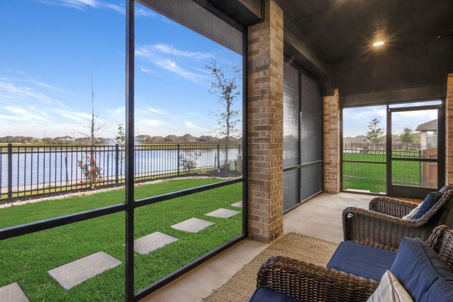 This photo shows a cozy screened-in porch overlooking a scenic lake. The space features brick pillars, a well-maintained lawn with stepping stones, and a serene view of the water through a metal fence. Ideal for relaxation and enjoying the outdoors.