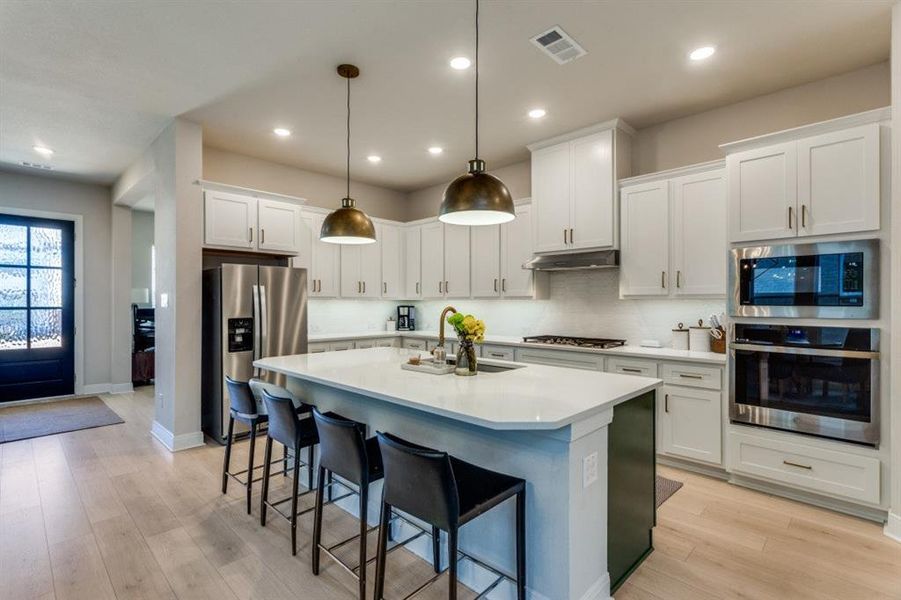 Kitchen with a center island with sink, visible vents, appliances with stainless steel finishes, a sink, and under cabinet range hood