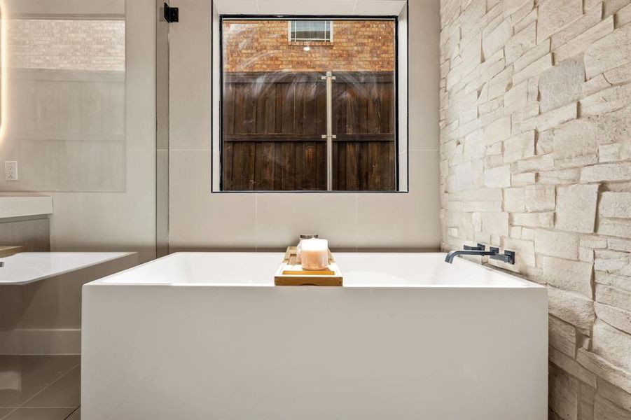 Contemporary soaking tub with a matte black wall-mounted faucet, complemented by a textured stone accent wall