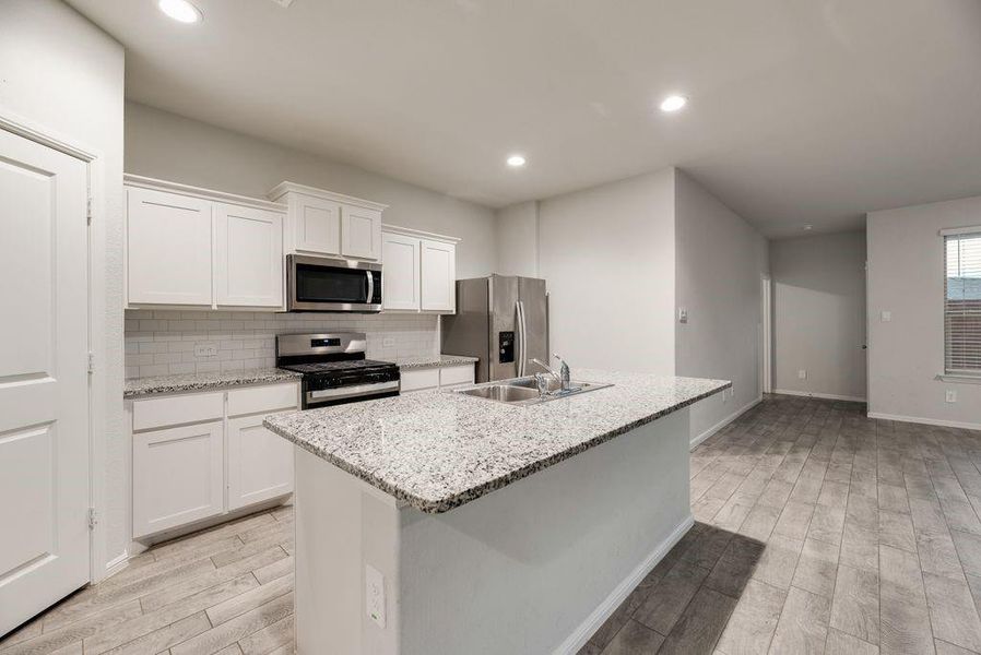 Kitchen featuring a central island with an undermount sink, stainless steel appliances, white subway tile backsplash, white cabinetry, and wood-finish flooring