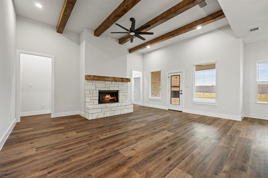 Unfurnished living room with dark wood-style flooring, visible vents, a stone fireplace, and baseboards