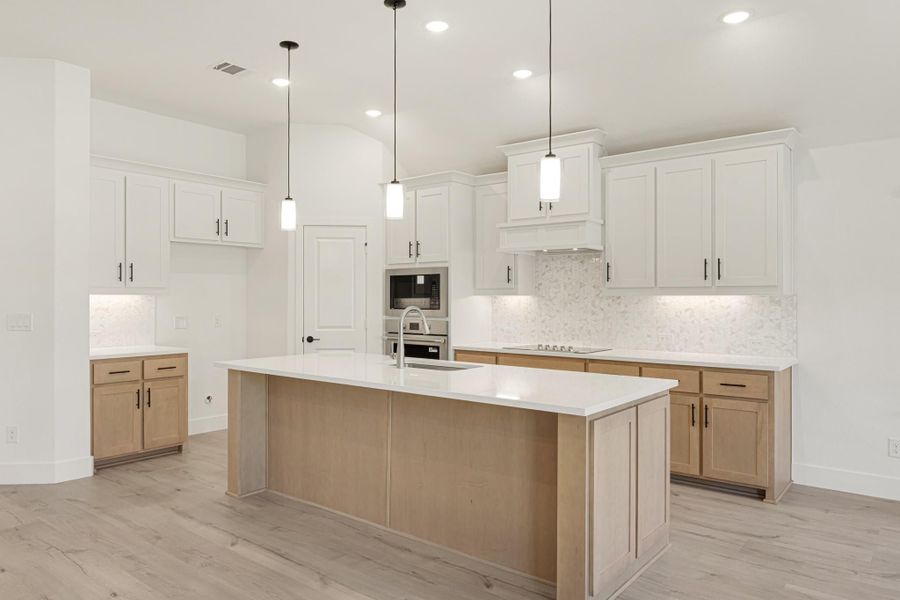 Kitchen with large center island, white upper cabinets, light wood lower cabinets, pendant lights, and stainless steel appliances