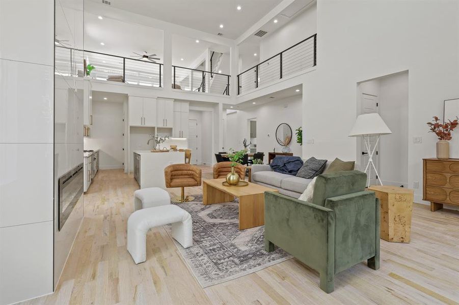 Living room featuring light wood-type flooring, wine cooler, ceiling fan, sink, and a high ceiling