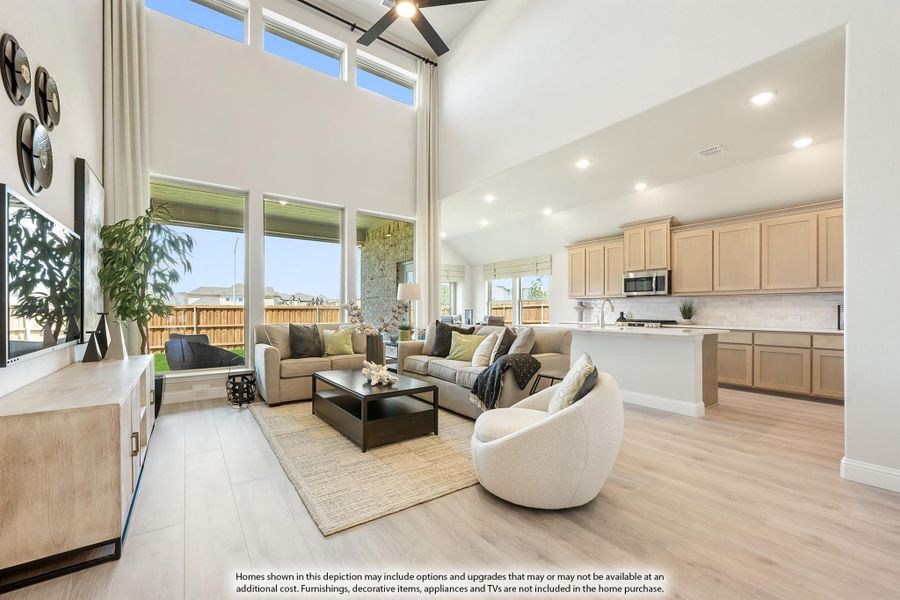 Open-concept living room with two-story ceilings, large windows, and adjoining kitchen with light wood cabinets