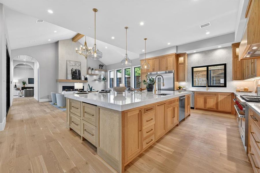 Spacious kitchen with a large central island, light wood-finish cabinetry, stainless steel appliances, and wood-finish flooring Spacious kitchen with a large central island, light wood-finish cabinetry, stainless steel appliances, and wood-finish flooring