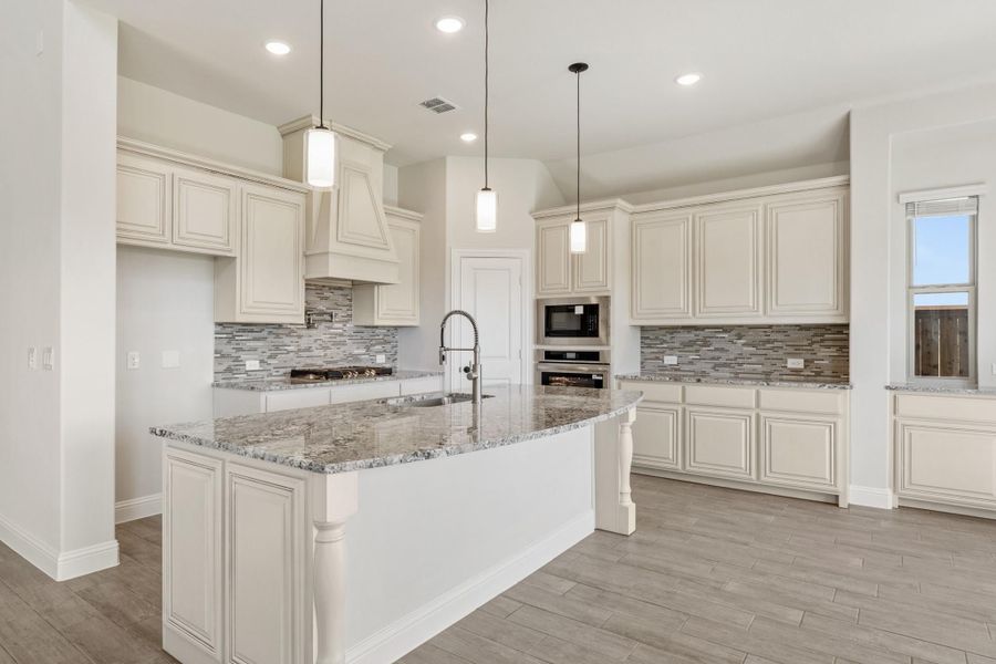 Kitchen with cream cabinets, granite island, tile backsplash, and pendant lights over large center island Kitchen with cream cabinets, granite island, tile backsplash, and pendant lights over large center island