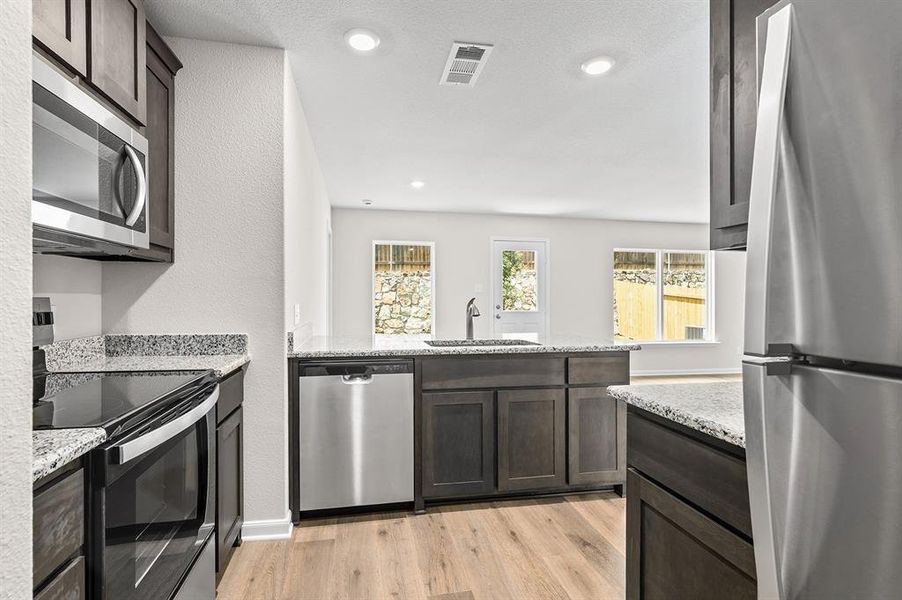 Kitchen featuring stainless steel appliances, light wood-style flooring, dark brown cabinets, light stone countertops, and a peninsula