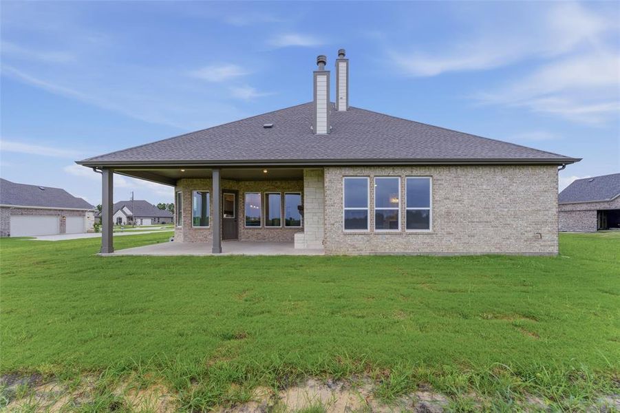 Expansive rear elevation featuring light brick masonry, a covered patio with recessed lighting, and multiple large windows