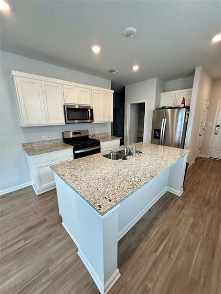 Kitchen featuring a large island with a double sink, white cabinetry, granite countertops, and wood-finish flooring