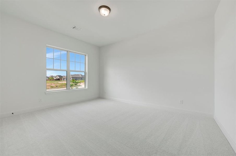 Room featuring light-toned carpeting, white walls, a large window with gridded panes, and a flush-mount ceiling light Room featuring light-toned carpeting, white walls, a large window with gridded panes, and a flush-mount ceiling light