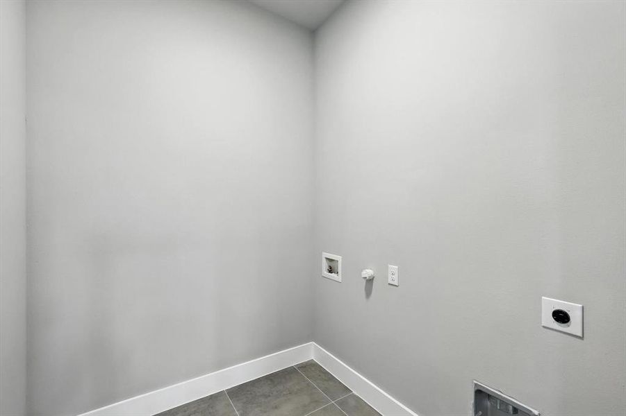 Laundry area with hookup for an electric dryer, hookup for a washing machine, dark tile patterned floors, and hookup for a gas dryer