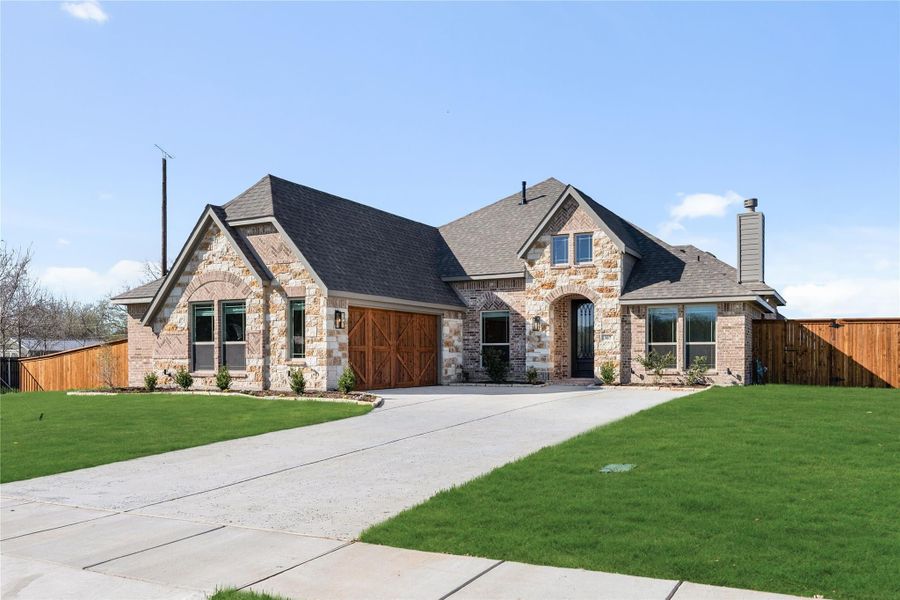 Single-story home with stone and brick exterior, two-car garage, arched entry, and green front lawn Single-story home with stone and brick exterior, two-car garage, arched entry, and green front lawn