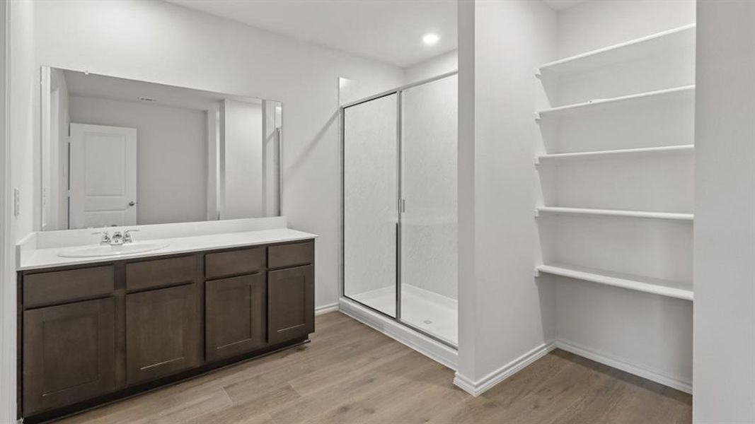 Bathroom featuring a vanity with a white countertop and undermount sink, dark wood-finish cabinetry, an expansive frameless mirror, a glass-enclosed shower, and built-in shelving