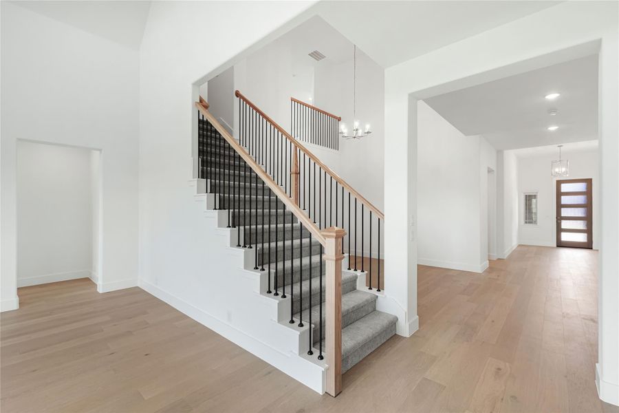Staircase with gray carpet, wood handrails, and black iron balusters in an open foyer with hardwood floors