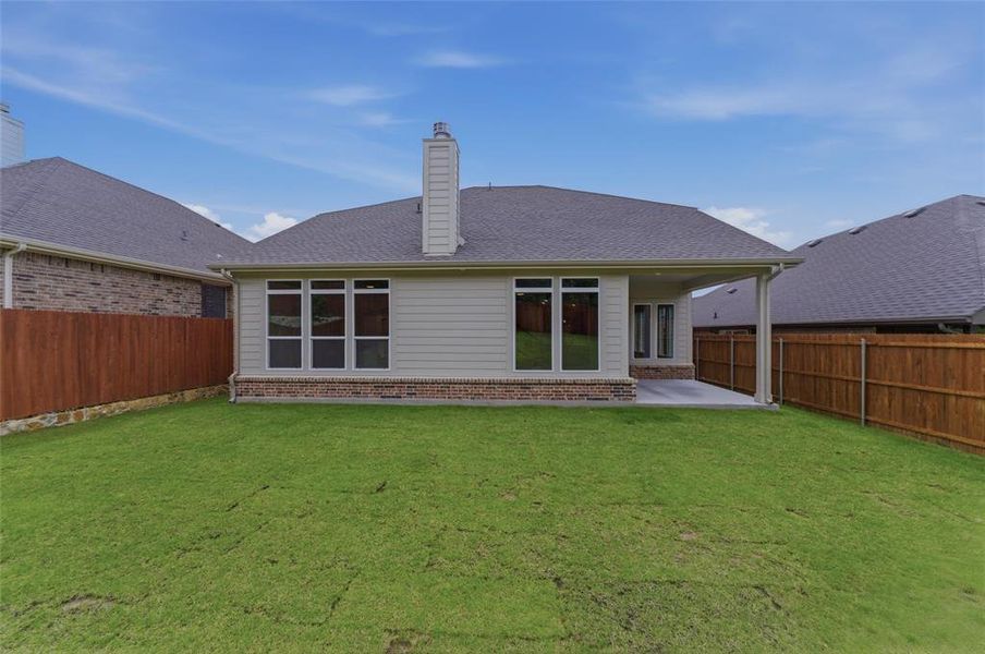 Expansive backyard featuring a manicured lawn, a full wooden privacy fence, and a covered concrete patio