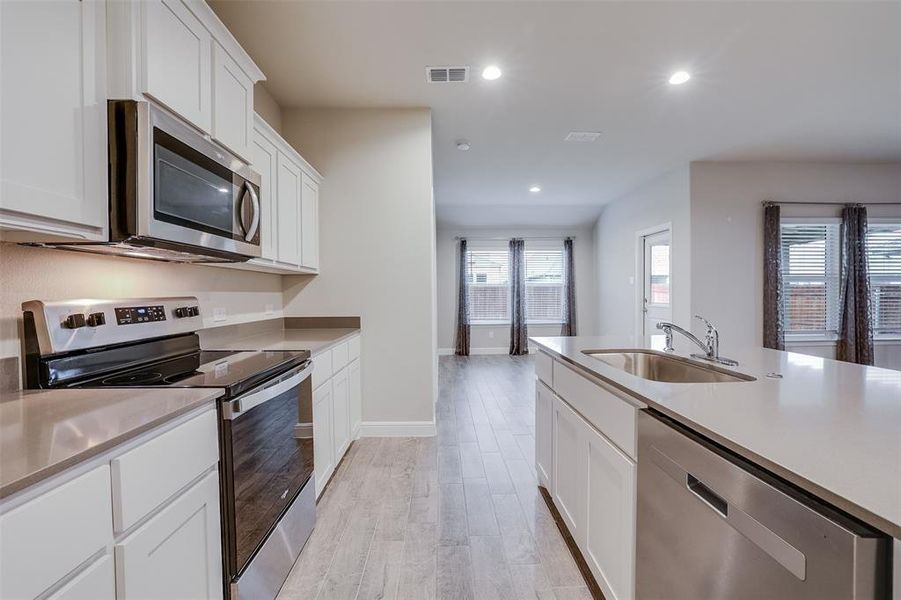 Kitchen with stainless steel appliances, white cabinets, recessed lighting, light wood-style flooring, and light stone counters Kitchen with stainless steel appliances, white cabinets, recessed lighting, light wood-style flooring, and light stone counters