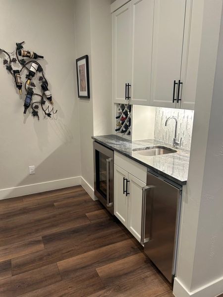 Indoor wet bar featuring white cabinetry, dark stone counters, dark wood-style flooring, and wine cooler Indoor wet bar featuring white cabinetry, dark stone counters, dark wood-style flooring, and wine cooler