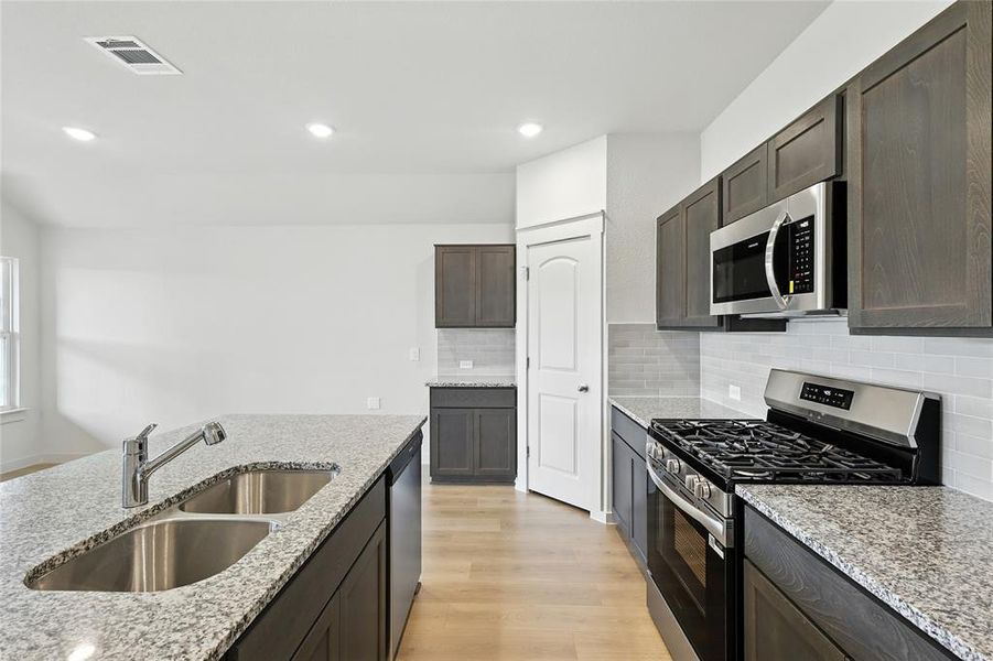 Kitchen with appliances with stainless steel finishes, light wood-type flooring, decorative backsplash, light stone countertops, and dark brown cabinetry Kitchen with appliances with stainless steel finishes, light wood-type flooring, decorative backsplash, light stone countertops, and dark brown cabinetry