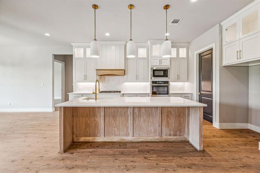 Kitchen featuring a kitchen island with sink, white cabinetry, oven, and light hardwood / wood-style flooring