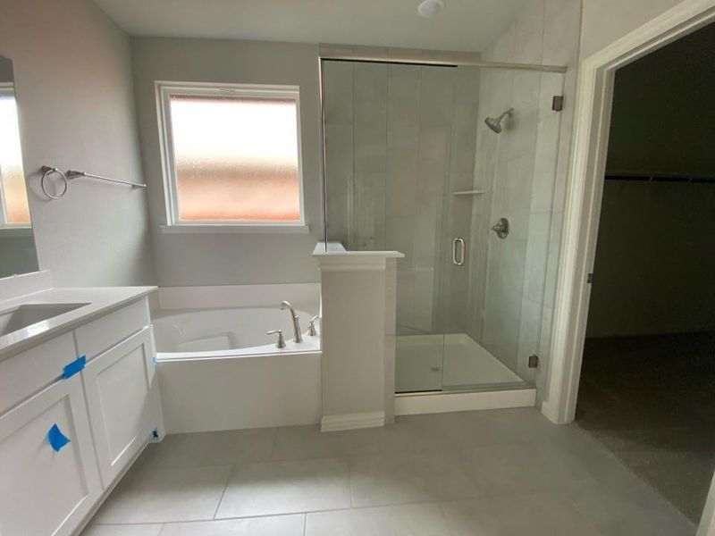 Contemporary bathroom featuring a white soaking tub, a frameless glass shower enclosure with a tile surround, a single vanity with a light-toned countertop, and large format tile flooring Contemporary bathroom featuring a white soaking tub, a frameless glass shower enclosure with a tile surround, a single vanity with a light-toned countertop, and large format tile flooring