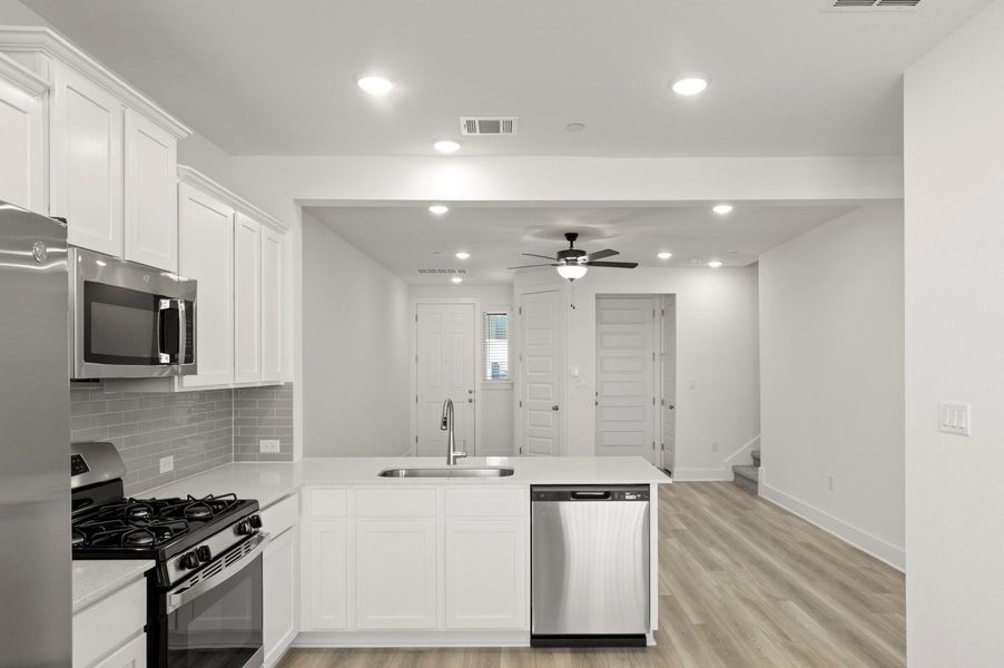 Kitchen featuring appliances with stainless steel finishes, white cabinets, a peninsula, backsplash, and ceiling fan