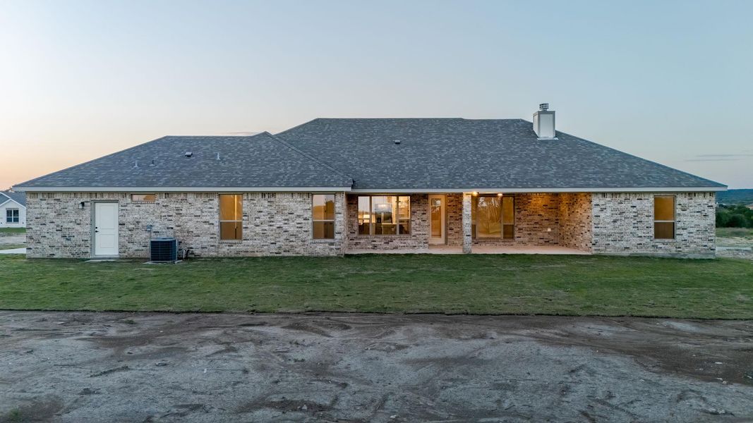 Back of property featuring a patio, a lawn, brick siding, a chimney, and roof with shingles Back of property featuring a patio, a lawn, brick siding, a chimney, and roof with shingles